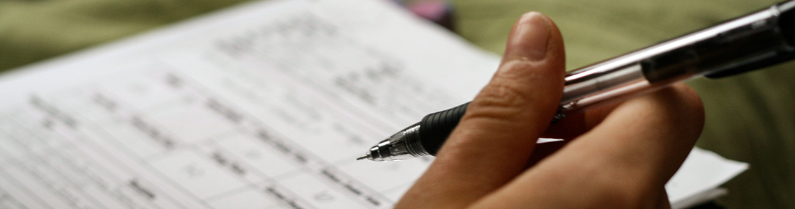 Una mano regge una penna davanti ad un foglio di carta