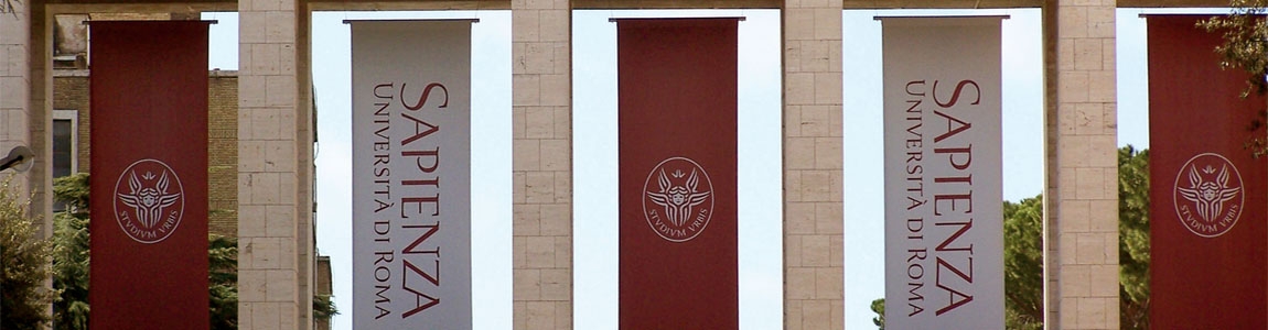 Entrata dei propilei siti all'Ingresso dell'Università di Roma La Sapienza con banner rappresentanti il logo universitario, un cherubino bianco su sfondo rosso e la scritta in verticale Sapienza