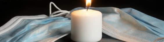L'immagine mostra una candela intorno alla quale sono presenti delle mascherine, come simbolo della commemorazione delle vittime COVID-19.